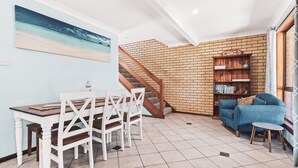 Un espacio de sala acogedor con una escalera, una mesa de comedor con sillas, un sofá azul y una estantería.