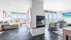 A modern living room with a fireplace, large windows, and a view of the ocean. - Gorgeous  Channelview Condo located on the ship channel in the heart of Port Ara (Port Aransas)