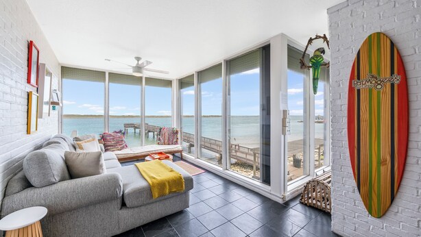A modern living room with a grey sofa, a yellow throw blanket, and a large window overlooking the beach. - Gorgeous  Channelview Condo located on the ship channel in the heart of Port Ara (Port Aransas)