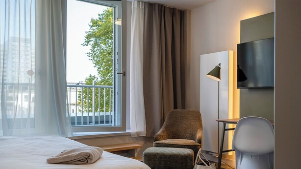 A hotel room with a bed, a chair, a desk, a TV, and a window with curtains. - HUB Apartments – St. Georg (Hamburg)