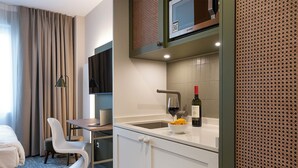 A hotel room with a bed, a desk with a laptop, a chair, a small kitchen area with a sink and a wine bottle. - HUB Apartments – St. Georg (Hamburg)