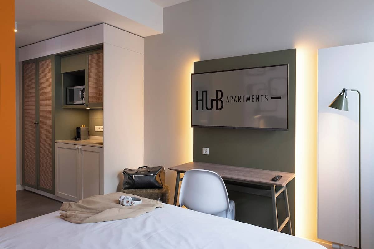 A modern hotel room with a bed, a desk, a chair, a TV, and a wardrobe.
