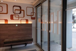A reception area with a wooden bench, a wall with geometric patterns, and a glass door. - HUB Apartments – St. Georg (Hamburg)