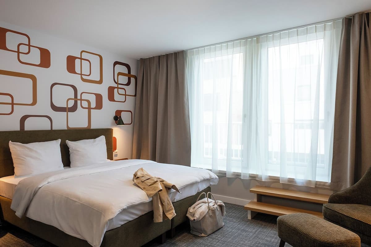 A hotel room with a bed, a bench, a chair, and a wall with geometric patterns.