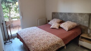 A bedroom with a bed, a nightstand, a lamp, a radiator, and a sliding door to a balcony.