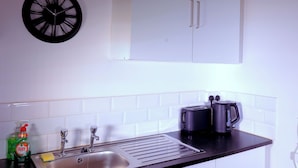 A kitchen with a white cabinet, a black clock, a sink, a toaster, and a kettle.