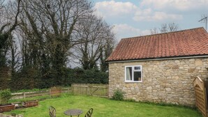 A stone house with a tiled roof, a fenced yard, and a small table with chairs. - Walnut Cottage (York)