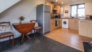 A compact kitchen with a refrigerator, oven, washing machine, and wooden cabinets. - Walnut Cottage (York)