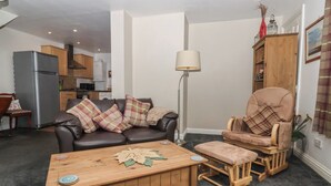 A living room with a sofa, a wooden coffee table, a rocking chair, a floor lamp, and a kitchen in the background. - Walnut Cottage (York)