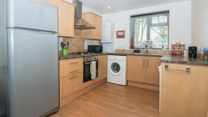 A modern kitchen with a stainless steel refrigerator, wooden cabinets, a microwave, a stove, an oven, and a washing machine. - Walnut Cottage (York)