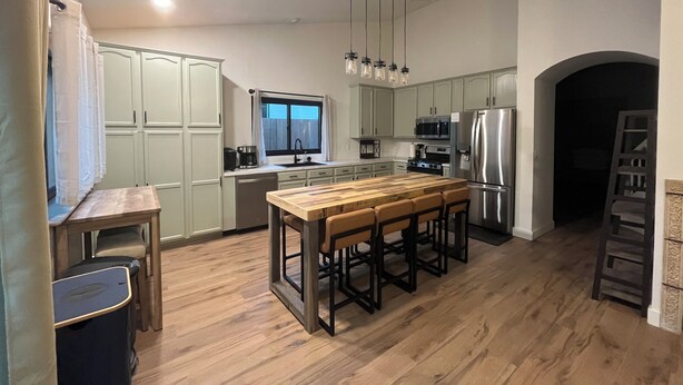 A modern kitchen with wooden flooring, a central island with bar stools, stainless steel appliances, and pendant lighting. - *Just Listed* Alpine Retreat with A/C and hot Tub! (Flagstaff)