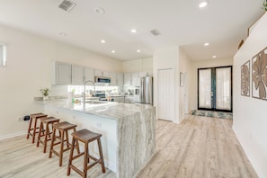 A modern kitchen with a marble island, wooden bar stools, and stainless steel appliances.