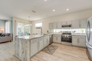 A modern kitchen with white cabinets, a marble island, stainless steel appliances, and a view to the outdoors.