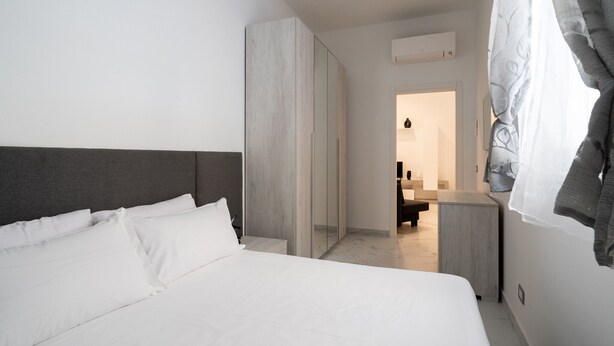 A modern hotel room with a large bed, a wardrobe, and a bathroom visible through an open door.