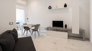 A modern living room with a sofa, a dining table with chairs, a flat-screen TV, and a fireplace.