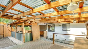 A wooden deck with a metal roof, a wooden bench, and a small outdoor area with a white wall and window. - 3 Mi to U of O Pet-friendly Home w/ Covered Deck! (Eugene)