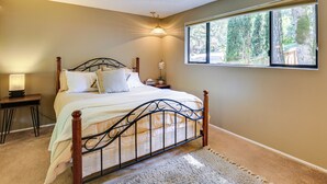 A bedroom with a bed, bedside table, lamp, and a window with a view of trees. - 3 Mi to U of O Pet-friendly Home w/ Covered Deck! (Eugene)
