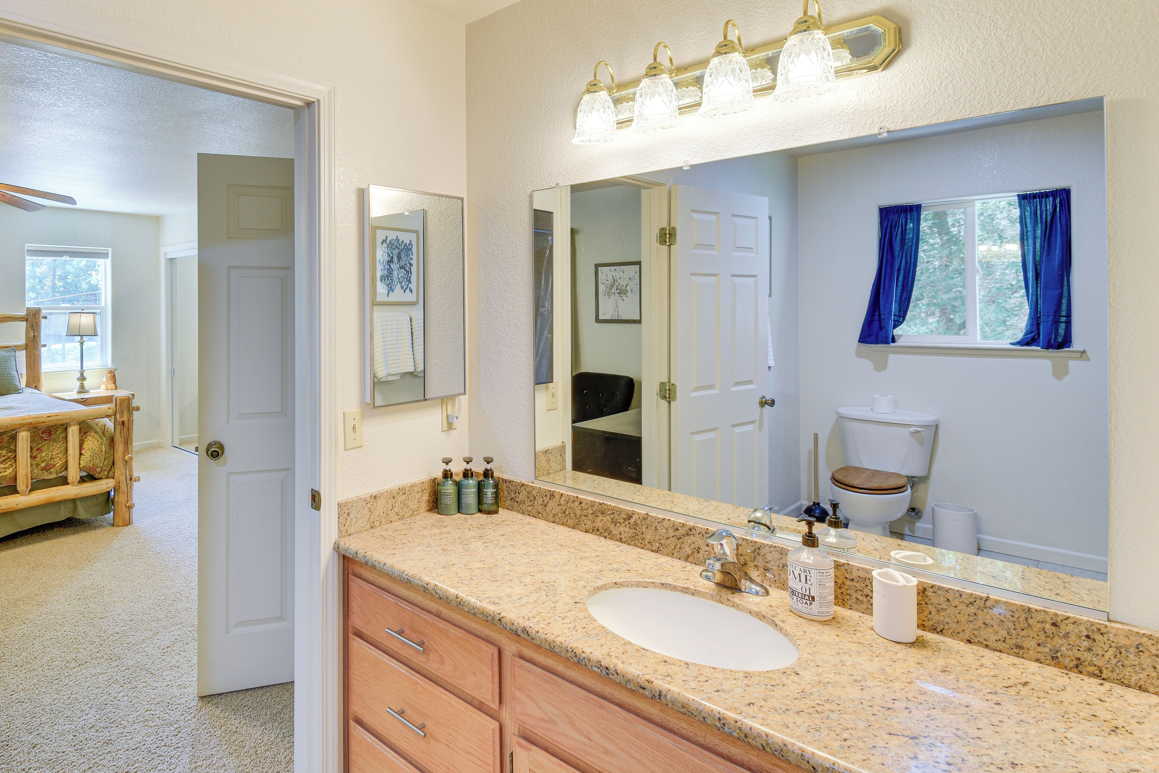 A bathroom with a granite countertop, a white sink, a large mirror, and a window with blue curtains.