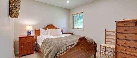 Une chambre à coucher avec un lit en bois, une table de chevet avec une lampe, une commode et une fenêtre donnant sur un paysage verdoyant.
