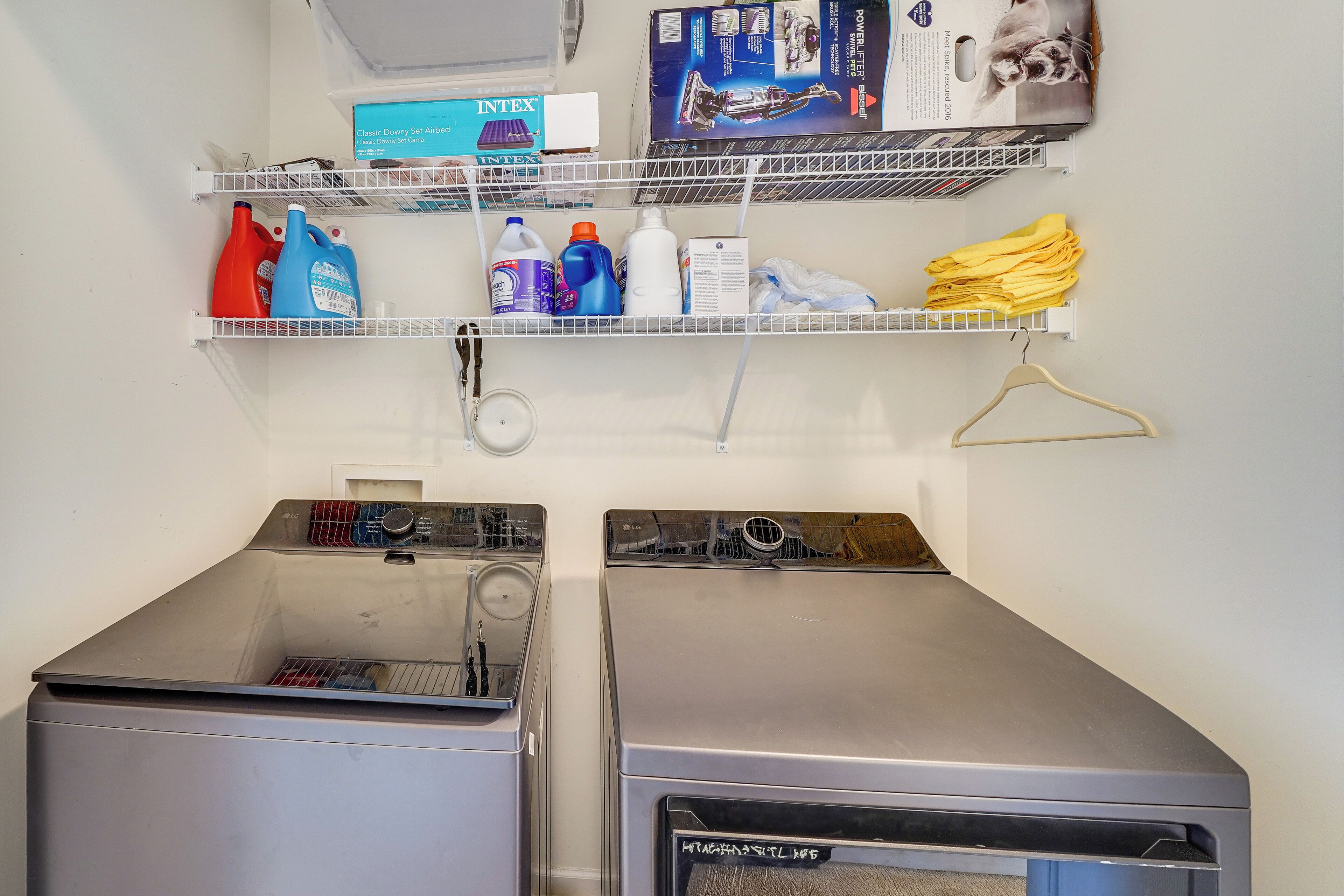 A laundry area with two washing machines, shelves with cleaning supplies, and a dryer.