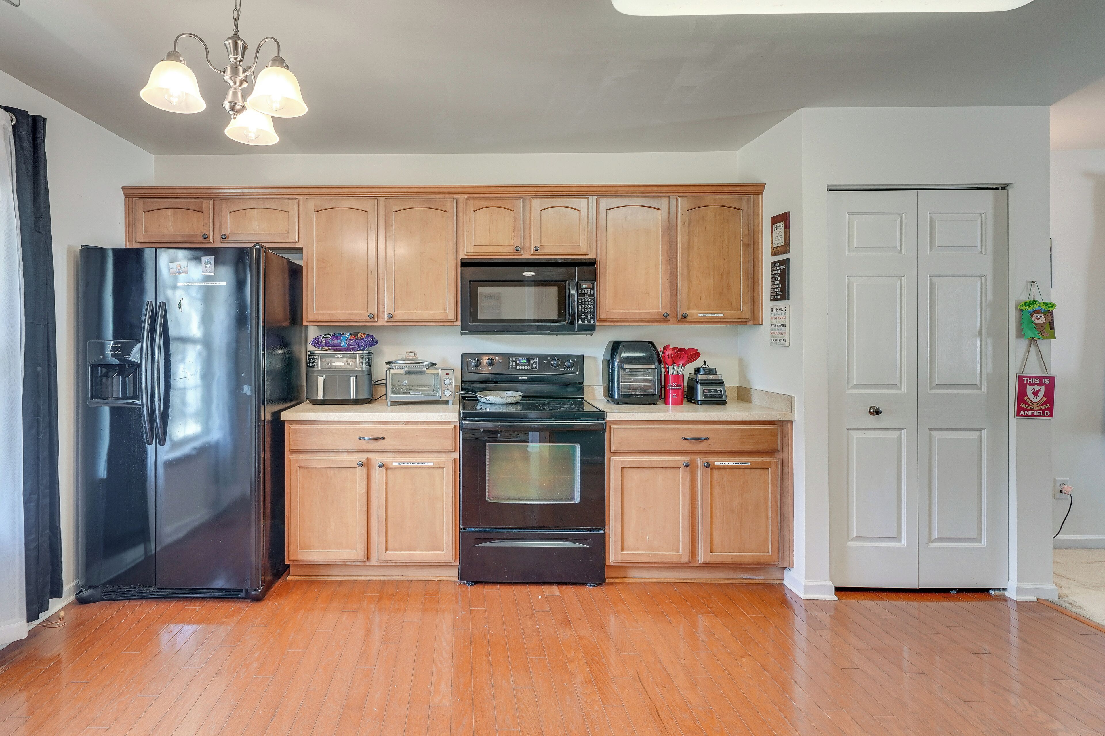 A kitchen with wooden cabinets, a black refrigerator, a microwave, a stove, and a coffee maker.