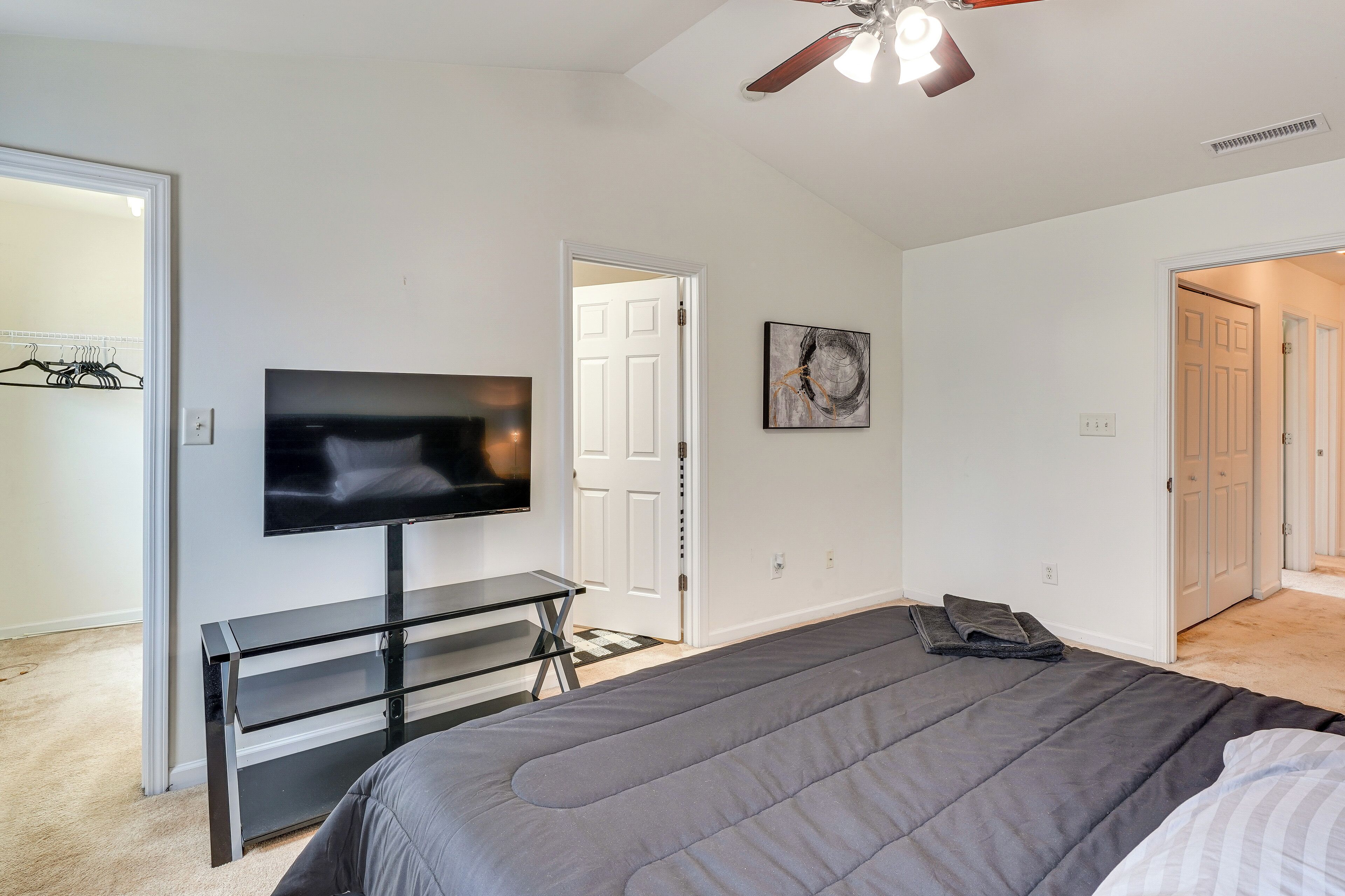 Une chambre à coucher avec un lit, un téléviseur posé sur un meuble, un ventilateur de plafond et une porte donnant sur une autre pièce.