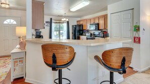 A kitchen with wooden cabinets, a central island with two bar stools, a refrigerator, microwave, and a toaster. - 6 Mi to Dtwn Raleigh: Townhome w/ Fenced Patio! (Raleigh)