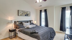 A bedroom with a large bed, a nightstand with a lamp, a painting on the wall, and a window with curtains. - 6 Mi to Dtwn Raleigh: Townhome w/ Fenced Patio! (Raleigh)