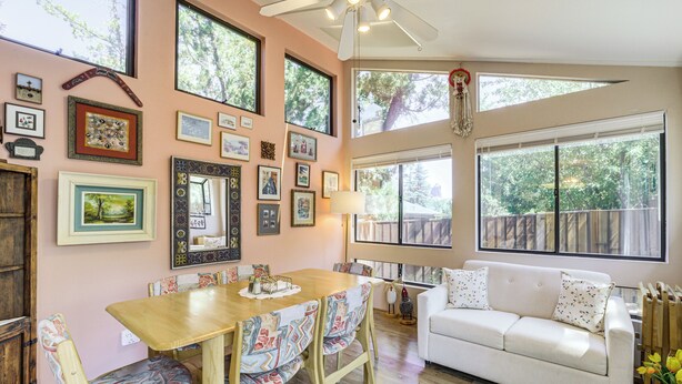 A dining area with a wooden table and chairs, a white sofa, and a large window with a view of trees. - Walkable Location! Extended Escape in Sedona (Sedona)