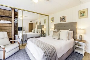 A hotel room with a large bed, a chair, a mirror, and a small table with a lamp.