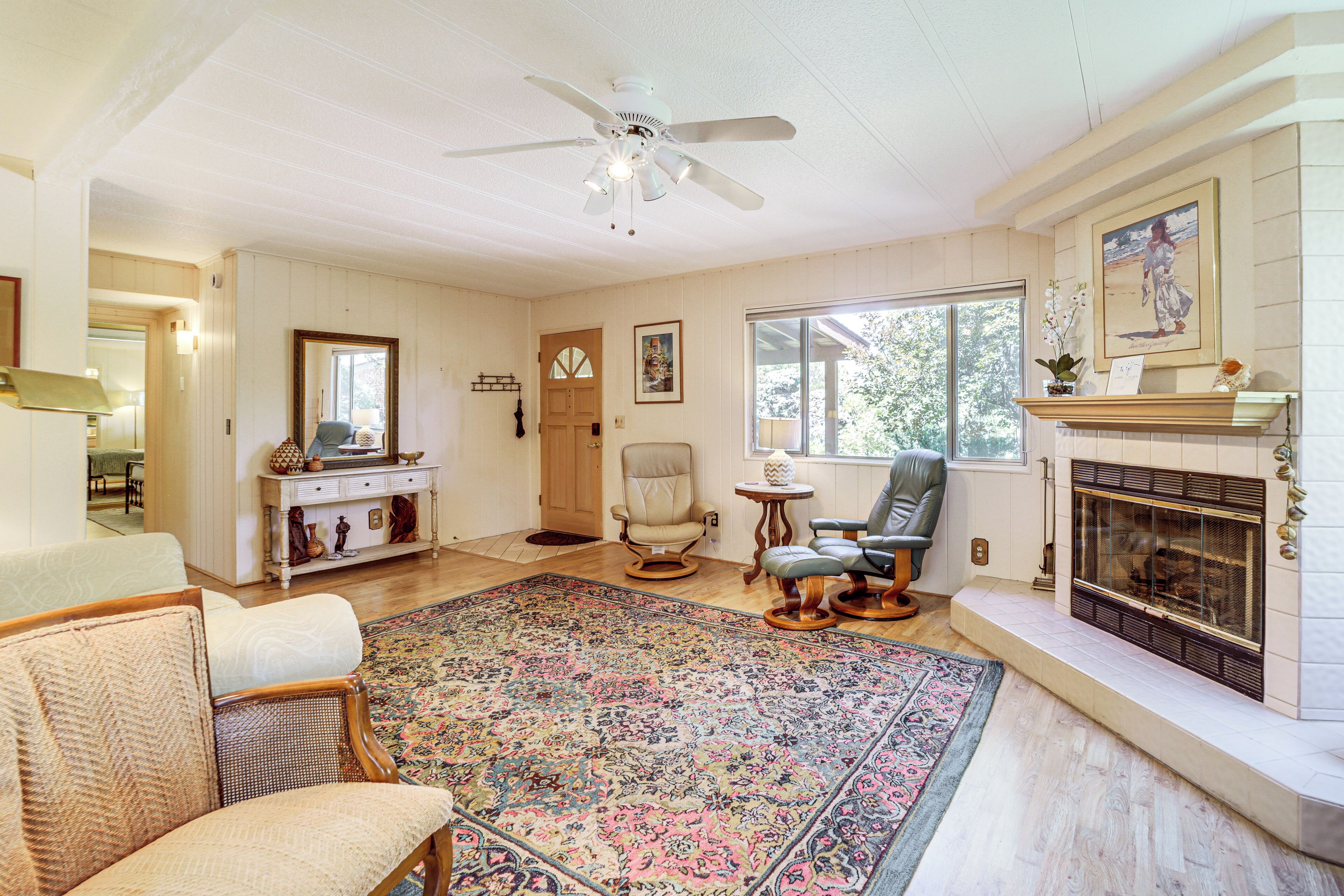 A spacious living room with a large rug, a fireplace, and a ceiling fan.