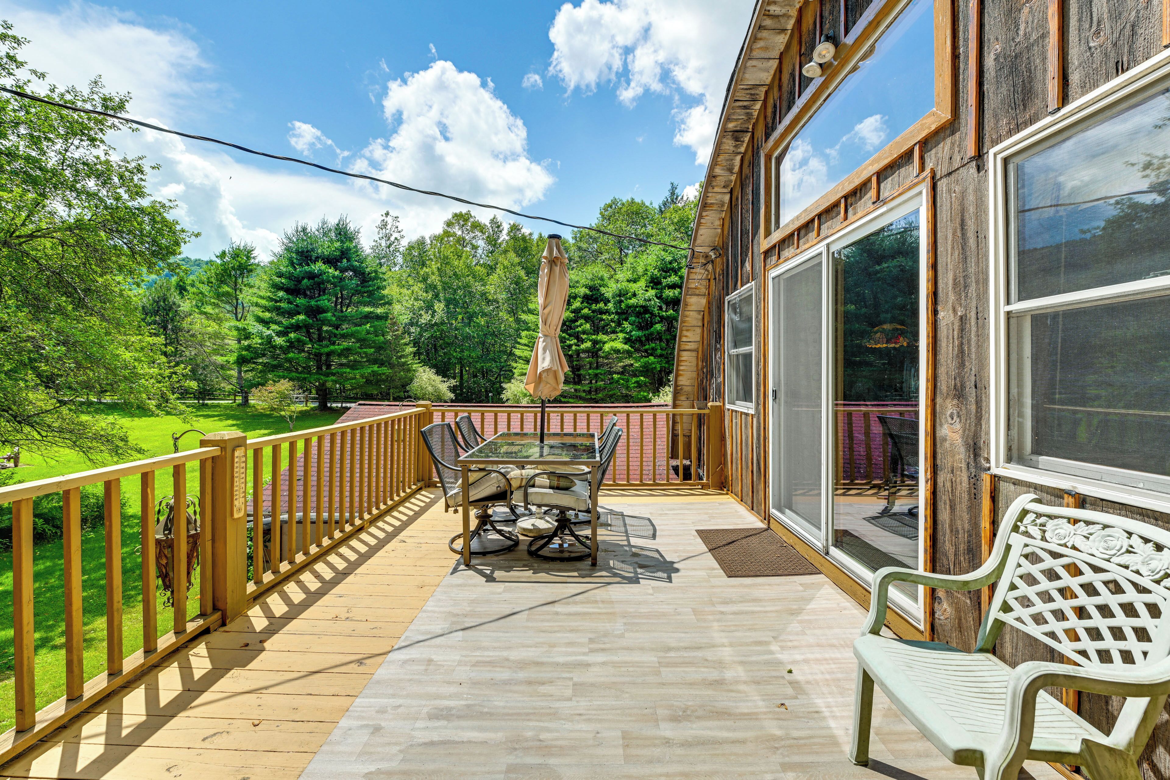 A wooden deck with a table and chairs, a bench, and a glass door leading to a patio area.