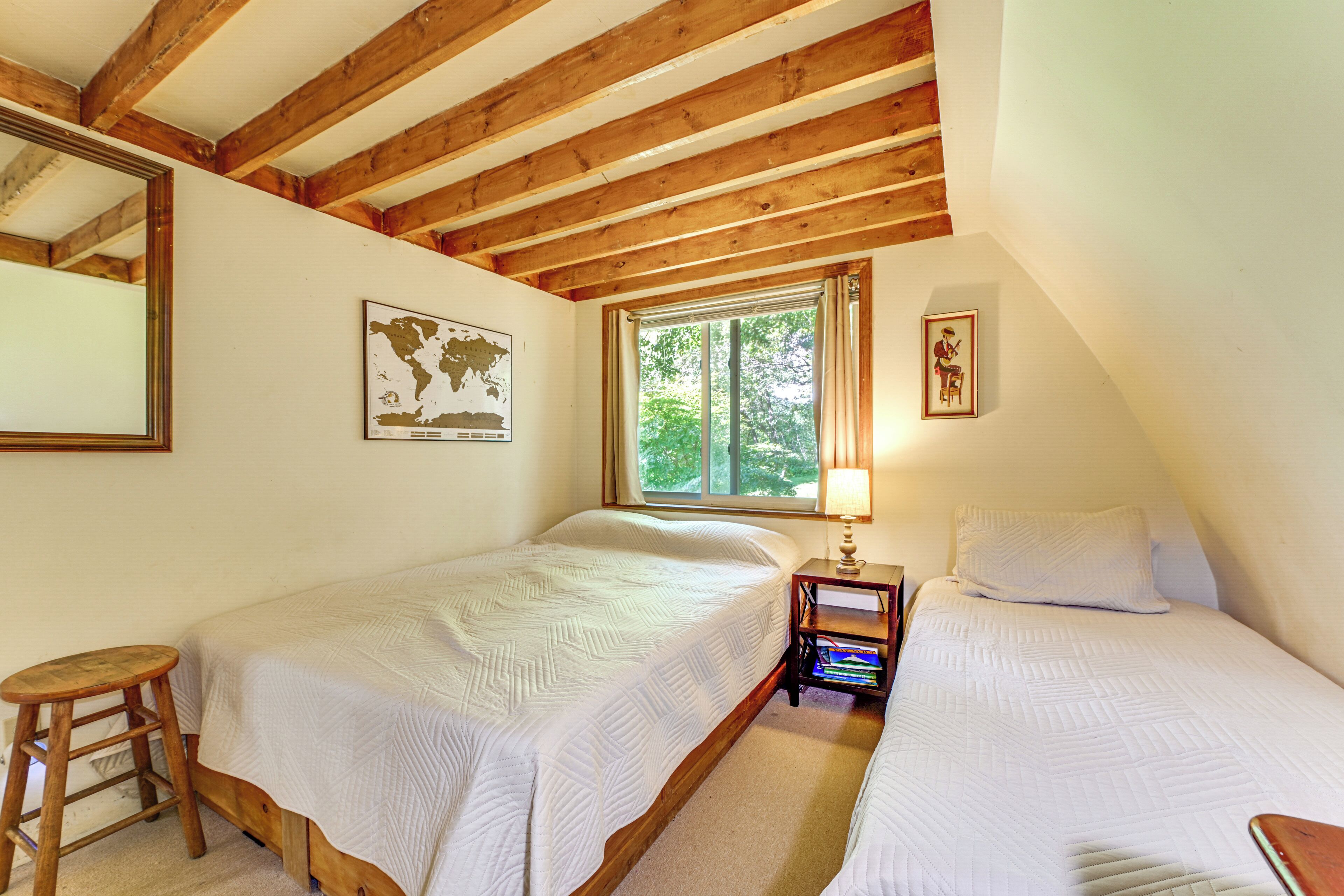 Une chambre avec deux lits, des poutres en bois, une fenêtre, une carte du monde et un tableau encadré au mur.