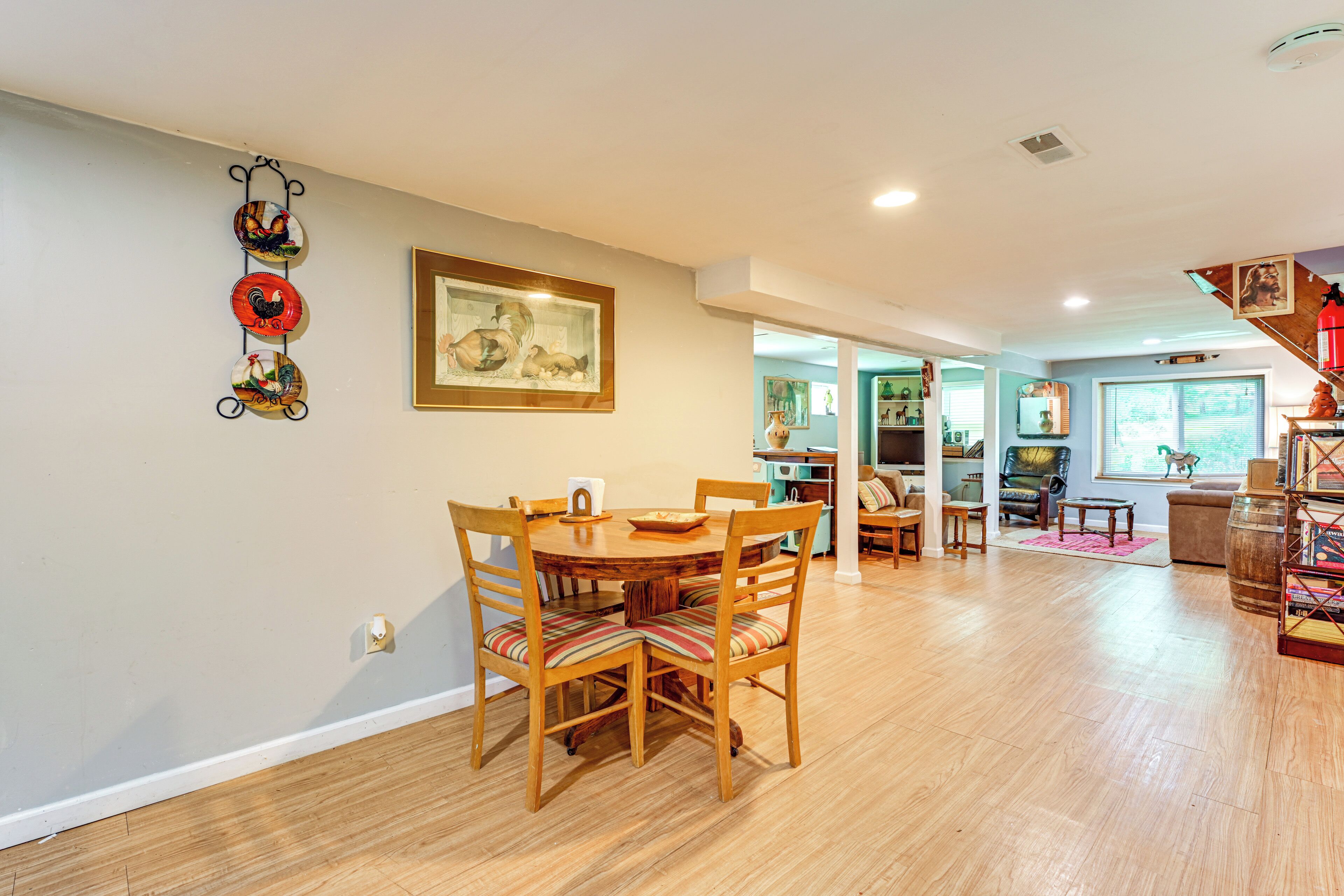 A dining area with a wooden table and chairs, a framed artwork on the wall, and a kitchen in the background.