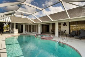 Une piscine avec un patio couvert, des chaises longues et un barbecue.