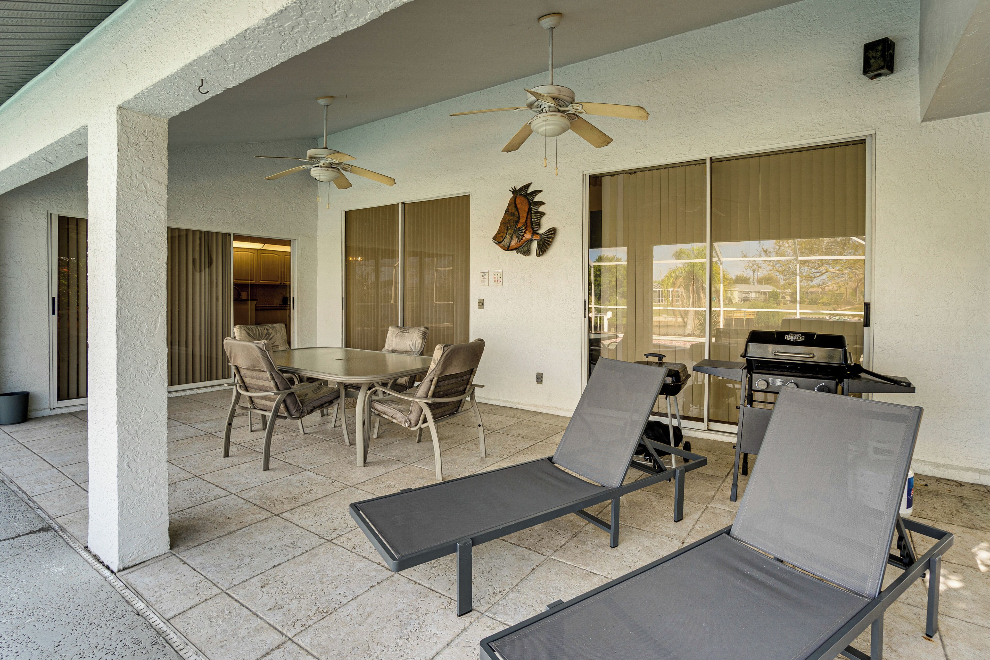 Eine Außenpatio mit Esstisch, Stühlen, zwei Lounge-Sesseln, Deckenventilatoren und einem Grill.