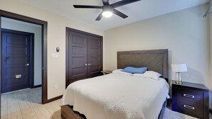 A bedroom with a bed, a ceiling fan, a nightstand, and a door.