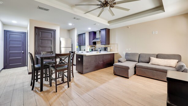 A modern living room with a dining area, a kitchen, and a ceiling fan.