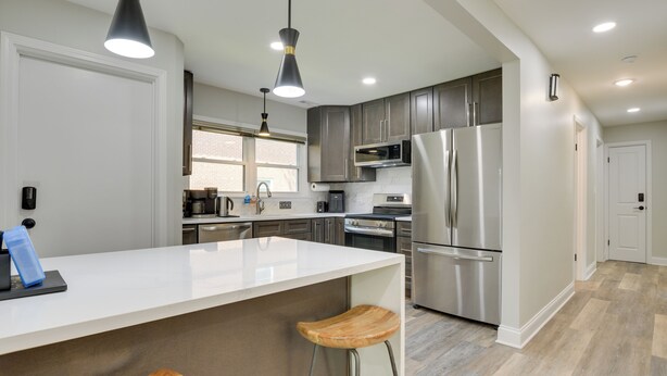Una cocina moderna con encimera blanca, electrodomésticos de acero inoxidable y taburetes de madera.
