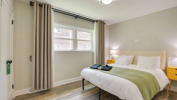 Una habitación de hotel con cama, mesita de noche, lámpara y ventana con cortinas.
