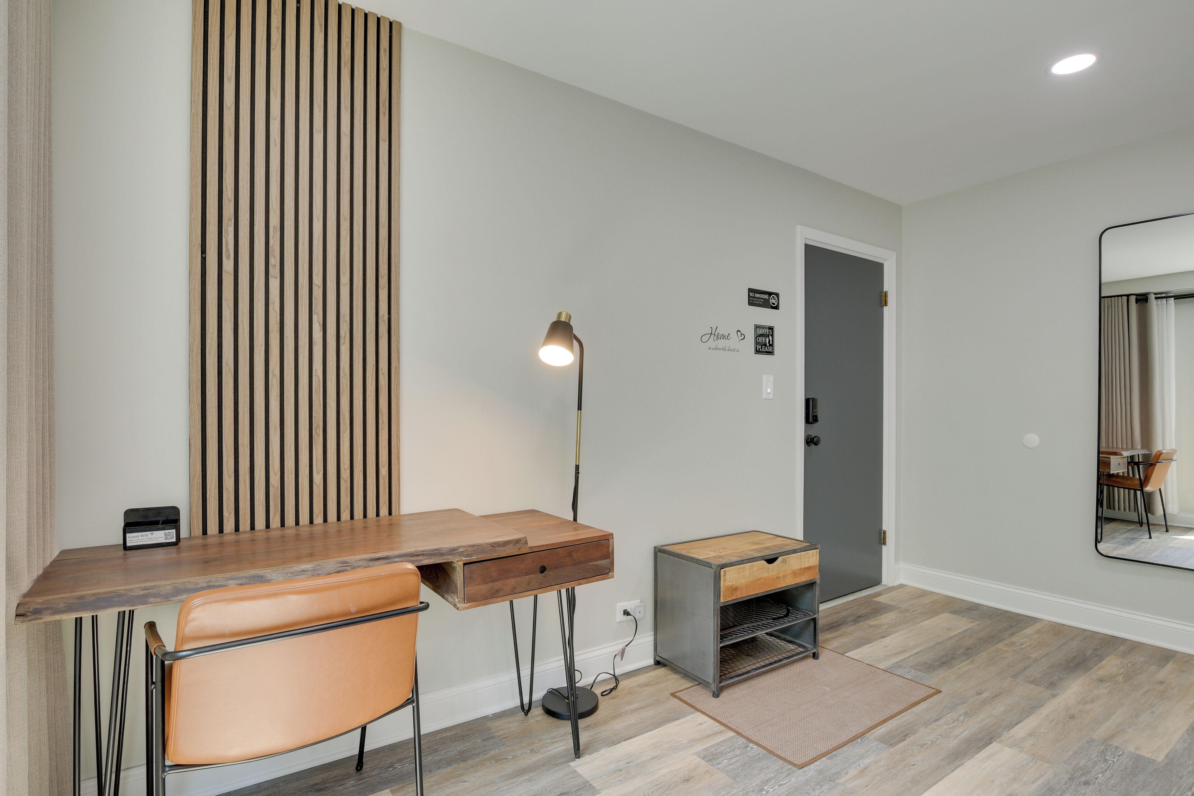 A modern room with a wooden desk, a chair, a lamp, and a small cabinet.