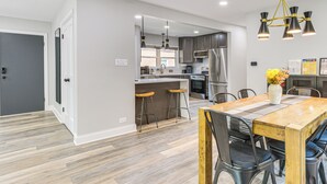 Una cocina moderna con electrodomésticos de acero inoxidable, una mesa de comedor de madera y taburetes de bar.