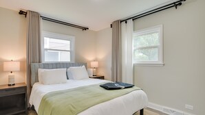 Una cama bien hecha con una manta verde, dos lámparas de noche y un ventanal con cortinas.