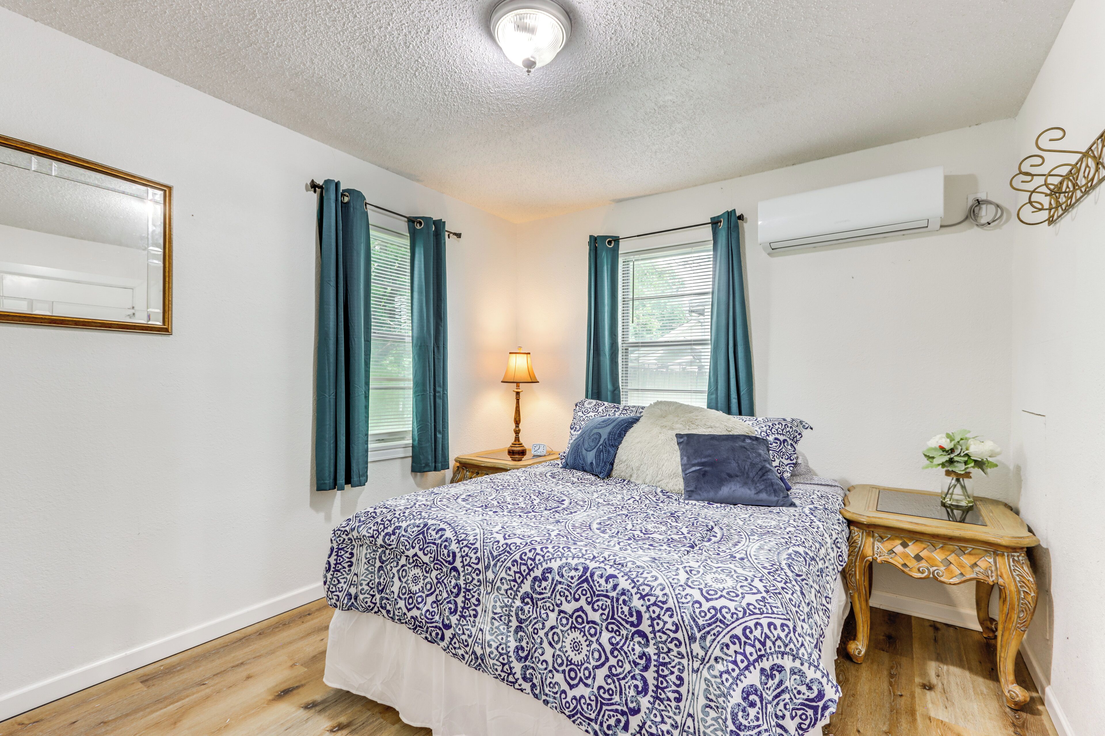 A bedroom with a patterned bedspread, a bedside table with a lamp, and a wall-mounted air conditioner.