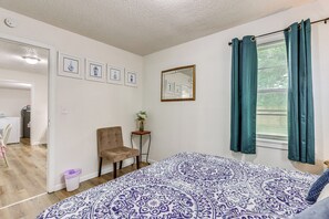 Une chambre à coucher avec une couvre-lit à motifs, une chaise, une petite table sur laquelle est posé un vase, et un miroir accroché au mur.