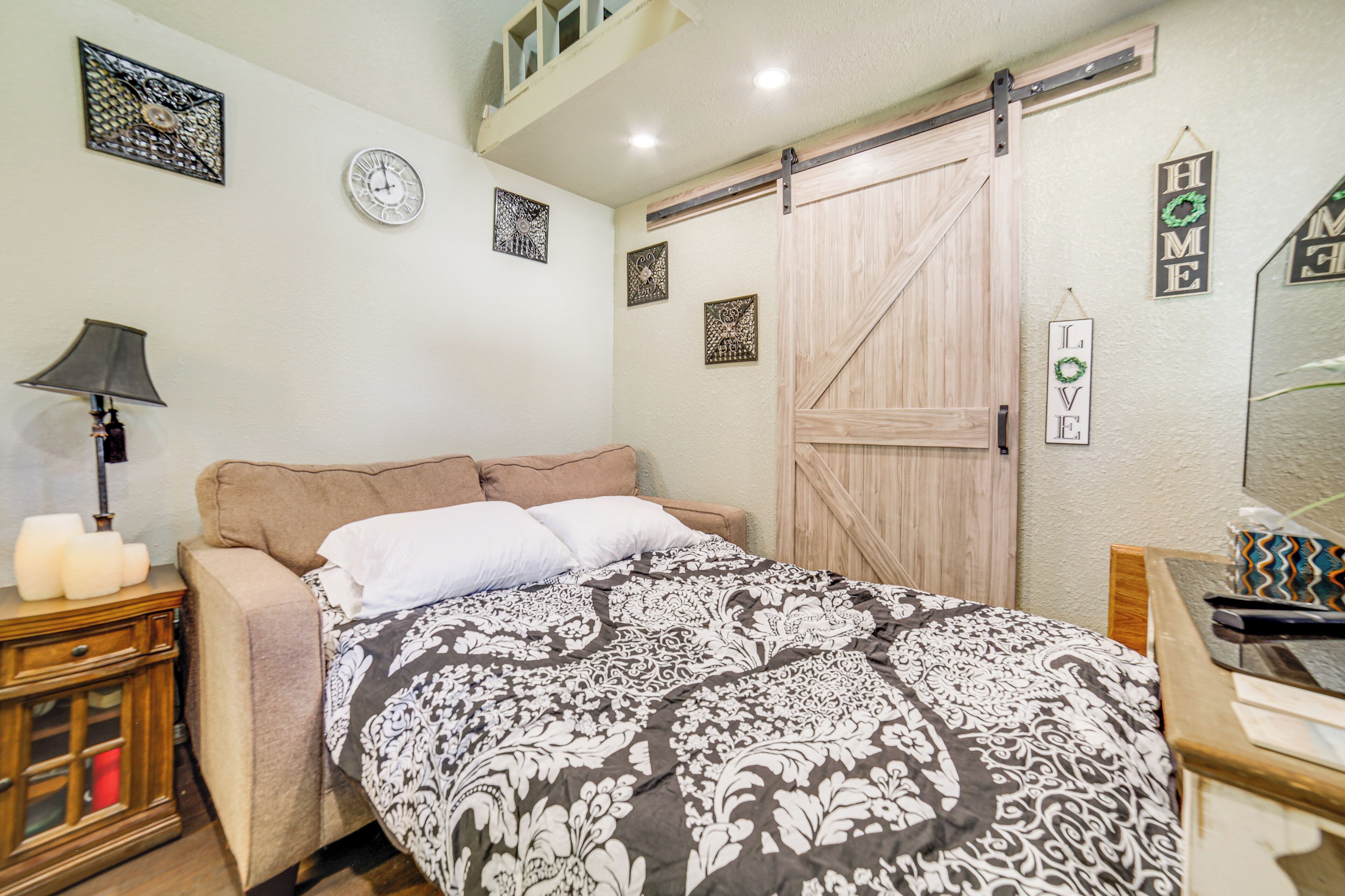 A bedroom with a bed, a nightstand, a dresser, a lamp, and decorative wall art.
