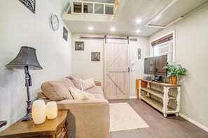 A cozy living room with a sofa, a coffee table, a lamp, a TV, and a sliding barn door. - Cozy Tiny Home: 1 Mi to The Village at Meridian (Meridian)