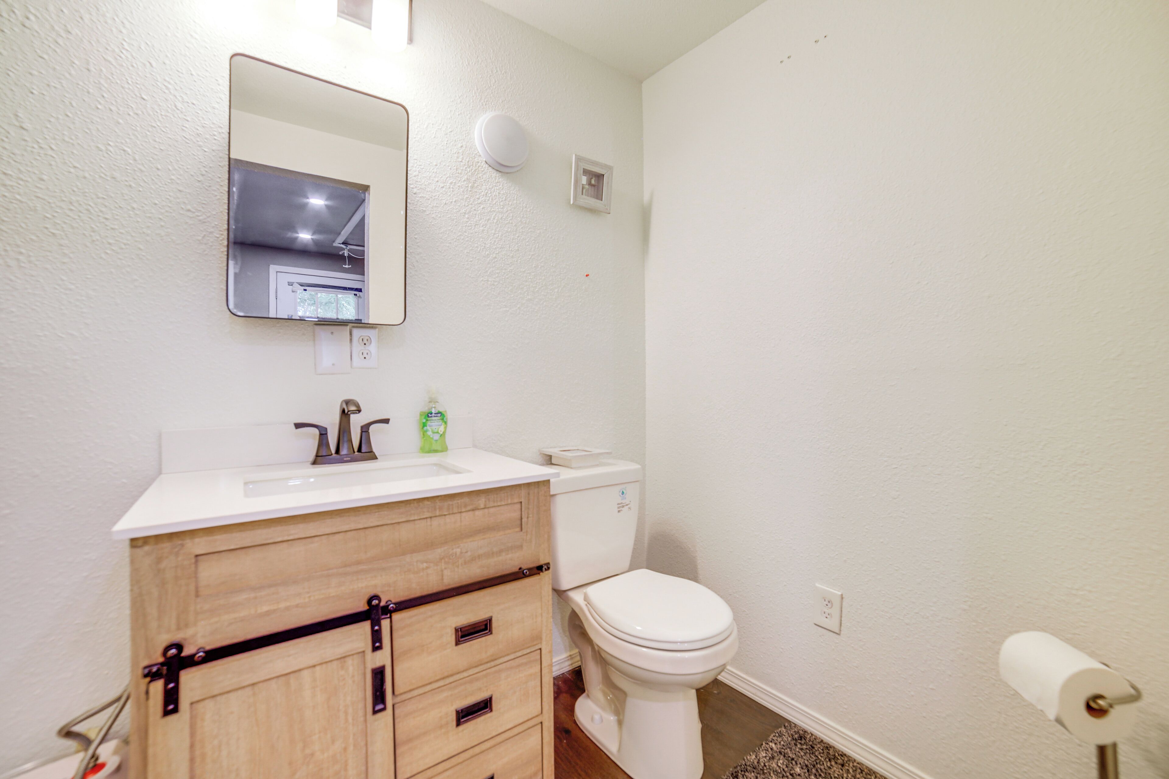 Un baño con lavamanos blanco, tocador de madera, inodoro y espejo.