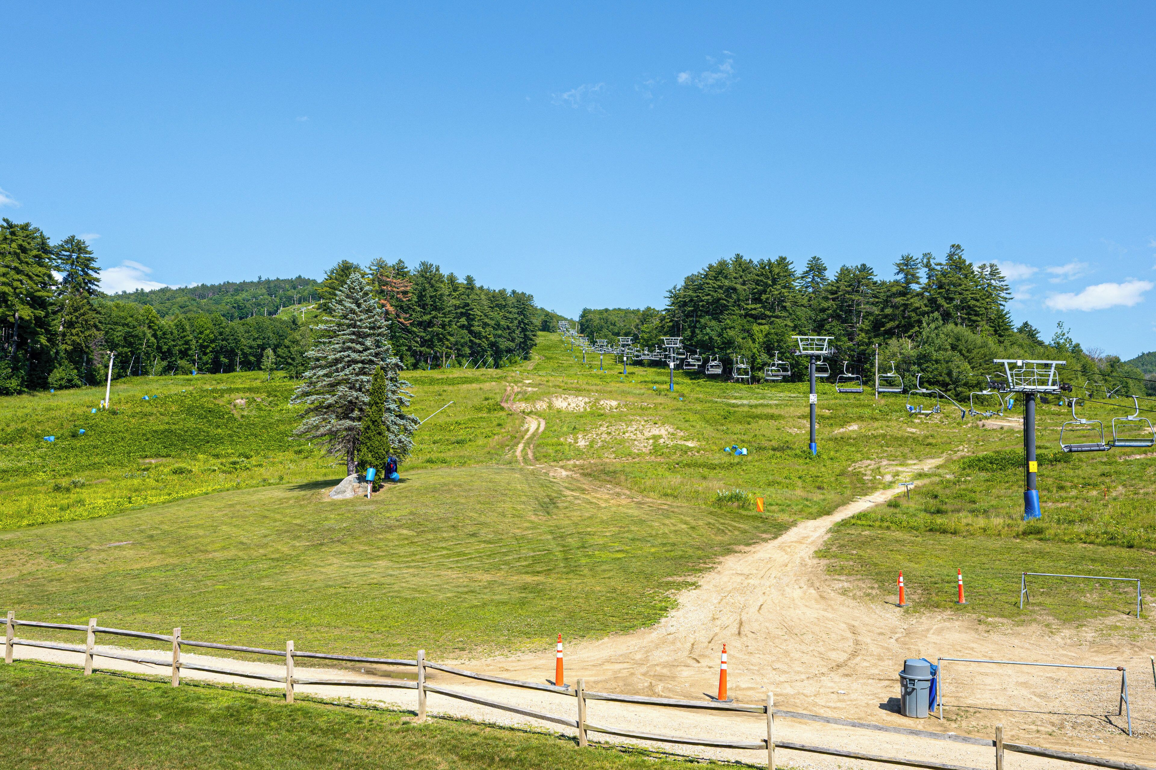 Une station de ski avec un chemin de terre menant à un télésiège, entourée d’arbres et de zones herbeuses.