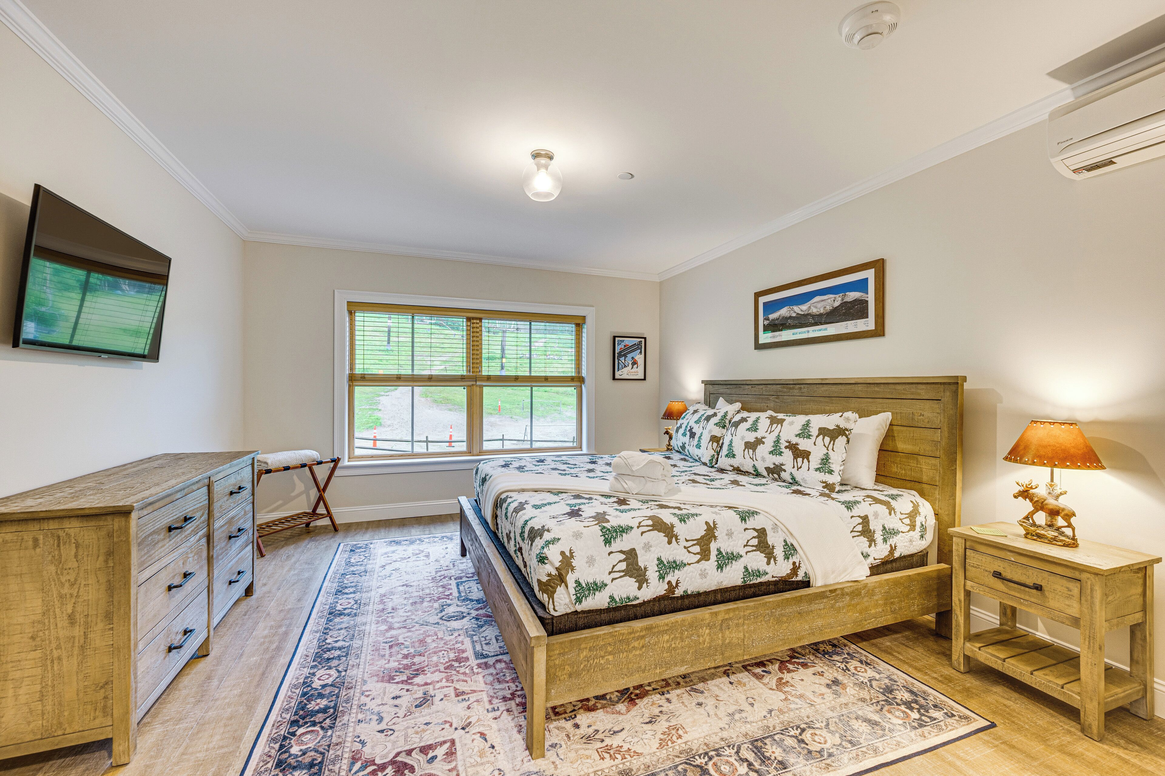 A bedroom with a bed, a nightstand, a dresser, a window, and a framed picture on the wall.